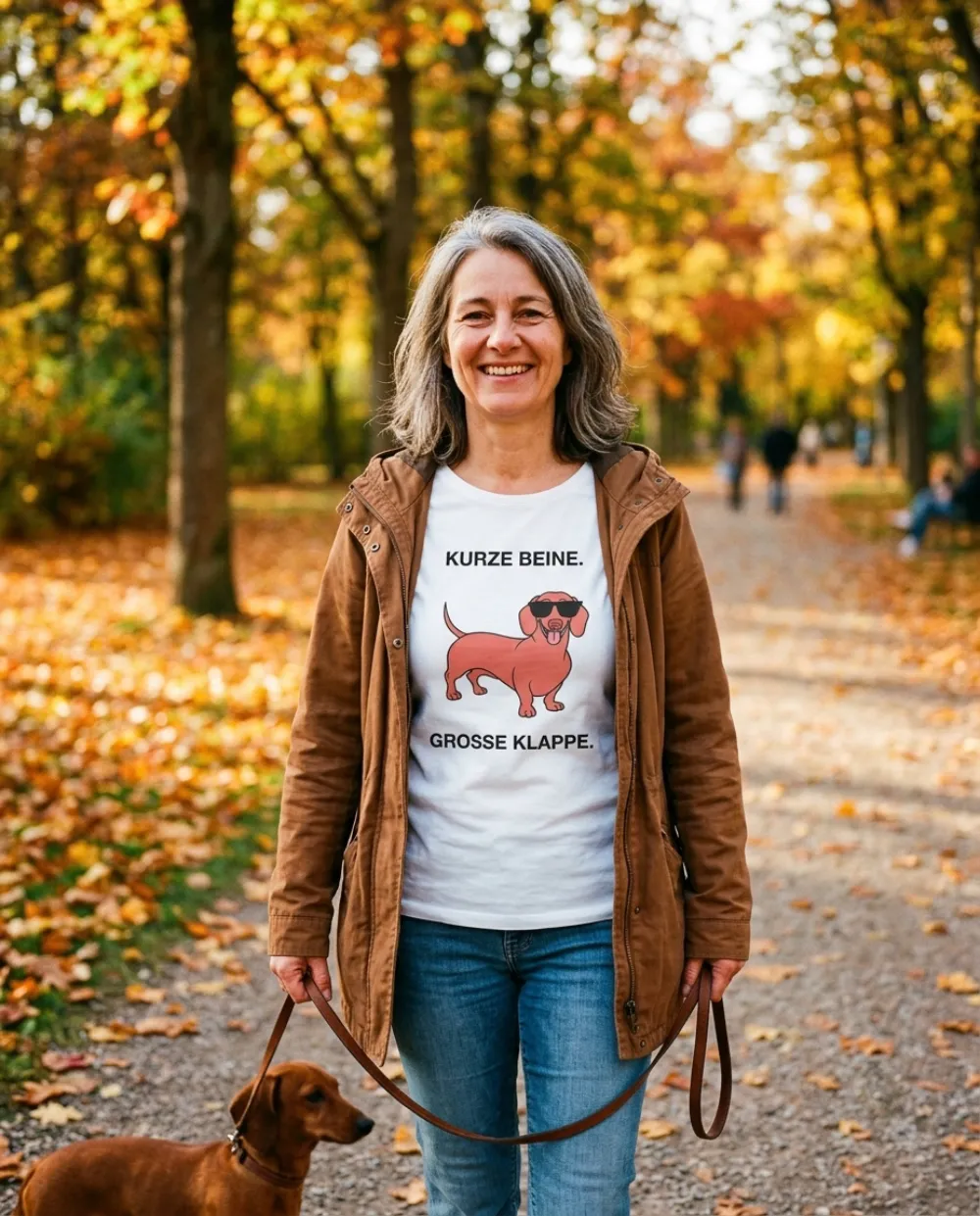 Frau im Herbstpark mit Dackel an der Leine, sie trägt das weiße T-Shirt „Kurze Beine. Große Klappe.“