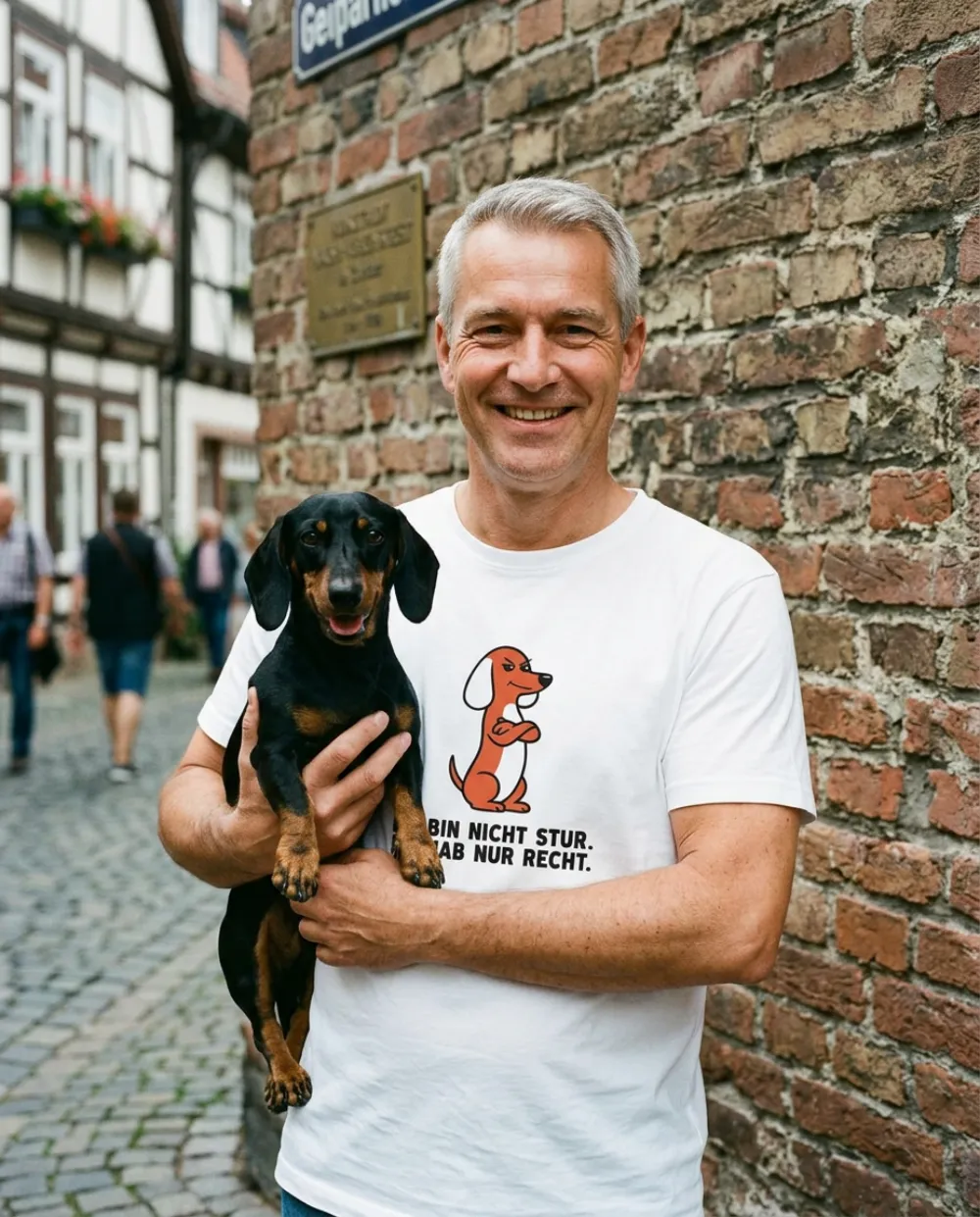 Lächelnder Mann in der Altstadt mit schwarz-braunem Dackel auf dem Arm, er trägt das T-Shirt „Ich bin nicht stur. Ich hab nur recht.“